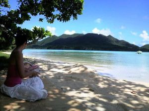 静かな湾を望む砂浜の木陰でゴザを敷いて、ヨガをする女性